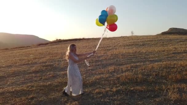 Happy cheerful girl with colorful balloons running across meadow at sunset on nature in summer. Drone view 4k - Πλάνα, βίντεο