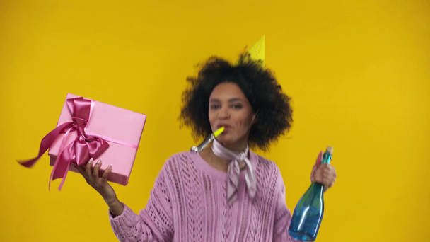 chica afroamericana con presente y botella aislada en amarillo
  - Metraje, vídeo