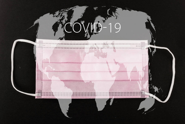 Covid-19テキストと世界地図で黒の背景に医療用保護マスク。外科用フェイスマスク。中国のコロナウイルス発生概念. - 写真・画像
