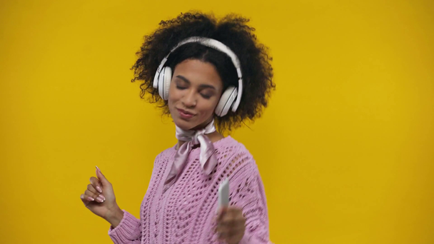 Afrykańska amerykańska dziewczyna tańczy i słucha muzyki odizolowanej na żółto  - Materiał filmowy, wideo