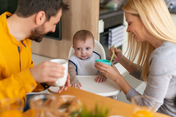Padre y madre alimentando a su pequeño bebé en casa.Familia, comida y bebida, amor y concepto de paternidad. - Foto, imagen