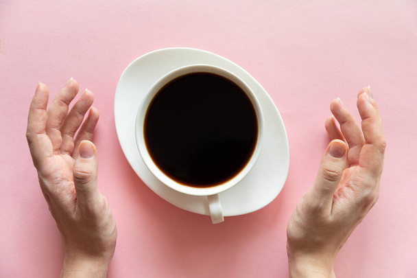 Nainen kädet ja kuppi kahvia vaaleanpunainen tausta, tasainen lay, ylhäältä näkymä
 - Valokuva, kuva