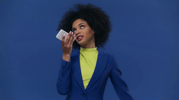 chica afroamericana usando teléfono inteligente aislado en azul
 - Metraje, vídeo