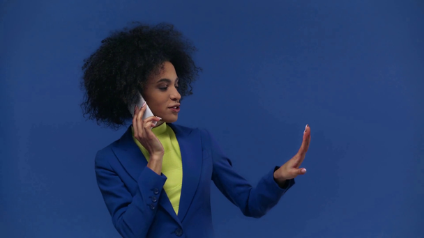 glücklich afrikanisch-amerikanisches Mädchen spricht auf Smartphone isoliert auf blau - Filmmaterial, Video