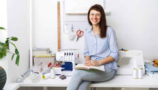 Cucire: Una donna d'affari di successo si siede sul suo posto di lavoro e prende appunti in un quaderno con un sorriso. Ritratto. - Foto, immagini