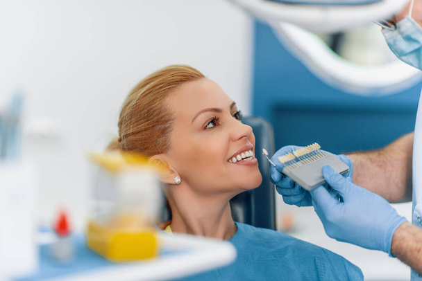 Az orvos összehasonlítja a beteg fogait a fogfehérítő táblázattal.Közelkép a páciens gyönyörű mosollyal a fogorvosnál. - Fotó, kép