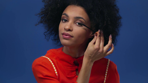 african american girl applying mascara isolated on blue - Záběry, video