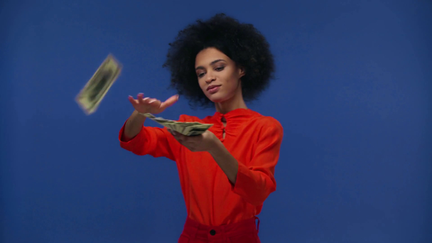 feliz afroamericano chica tirar dinero en el aire aislado en azul
 - Metraje, vídeo