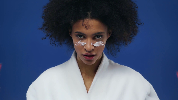 Afryki amerykanka dziewczyna stosowania krem do twarzy izolowane na niebiesko - Materiał filmowy, wideo