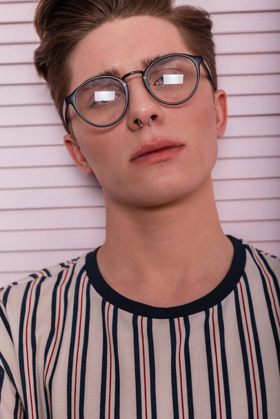 Portrét mladého atraktivního mužského hipstera s čistou zdravou pletí v módních brýlích se stylovým účesem v módním tričku v řadě u dřevěné vinobraní růžové stěny. Sexy modelka chlap ve studiu - Fotografie, Obrázek
