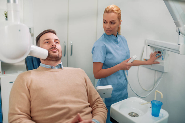 Οδοντίατρος προετοιμάσει για να κάνει το δόντι x-ray εικόνα για τον ασθενή στην οδοντιατρική κλινική.Άνθρωποι, ιατρική, στοματολογία και την υγειονομική περίθαλψη έννοια. - Φωτογραφία, εικόνα