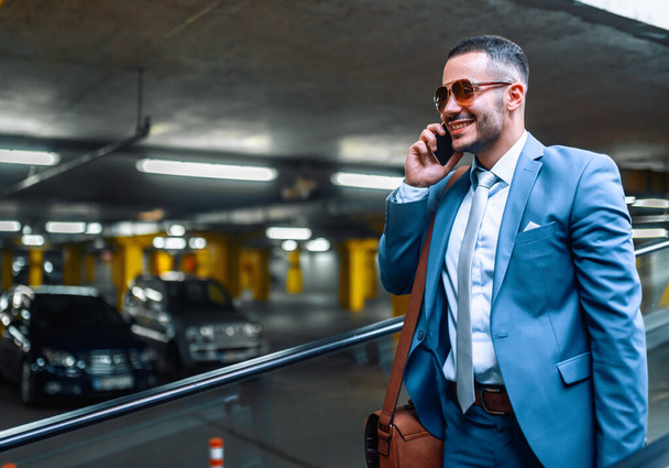 Atractivo joven empresario usando el teléfono inteligente.Retrato de hombre de negocios guapo al aire libre en la ciudad
. - Foto, imagen