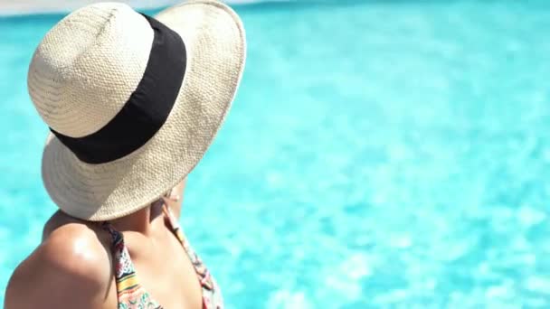 closeup beautiful Caucasian girl in hat sitting at pool edge on clear blue water background and sunbathing. - Záběry, video