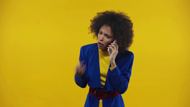 θυμωμένο αφροαμερικανό κορίτσι που μιλάει σε smartphone απομονωμένο στο κίτρινο - Πλάνα, βίντεο