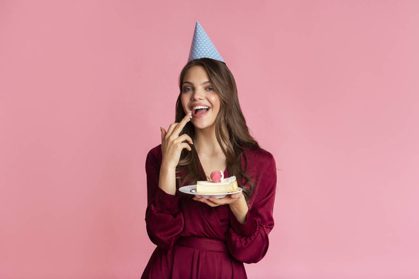 Cheerful Girl Licking Cream Of Birthday Cake In Her Hands - Foto, imagen