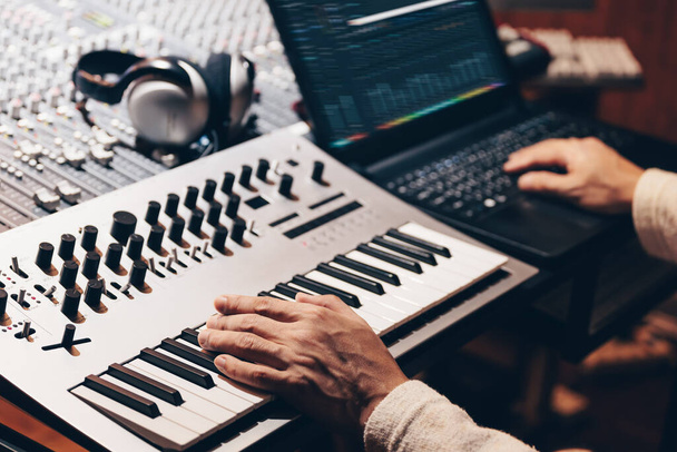 music producer hands composing a song on synthesizer keyboard and laptop computer in recording studio - 写真・画像