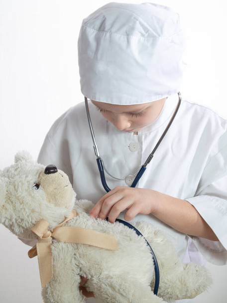 Cute kid boy playing doctor with plush toy at home. child boy playing doctor and curing plush toy indoors. isolated on white - Foto, afbeelding