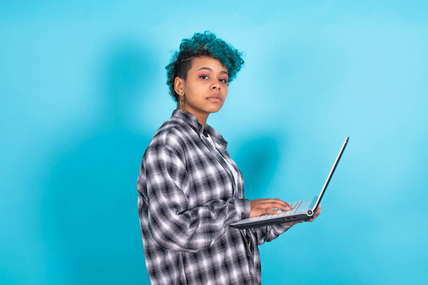 fiatal afro-amerikai nő kék göndör haj és laptop számítógép elszigetelt sárga háttér - Fotó, kép