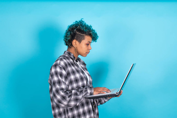 młoda Afroamerykanka z niebieskimi kręconymi włosami i laptopem odizolowany na żółtym tle - Zdjęcie, obraz