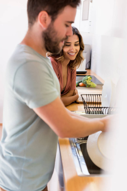 Dzielenie się obowiązkami domowymi. Szczęśliwa kobieta ogląda mężczyzn zmywających naczynia.  - Zdjęcie, obraz