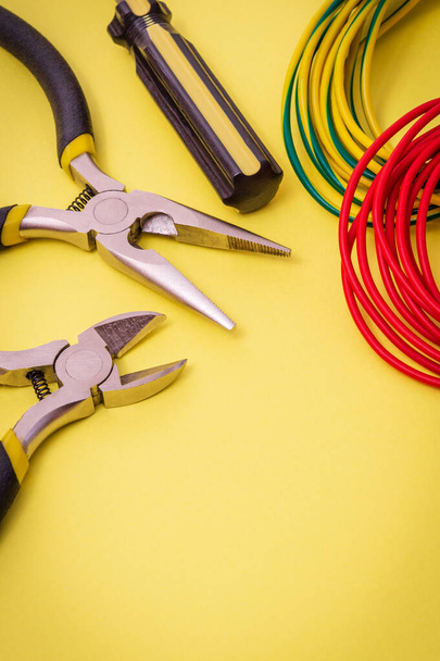 Electrician's tools and wire on a yellow background for repairing energized systems or communications - Photo, Image