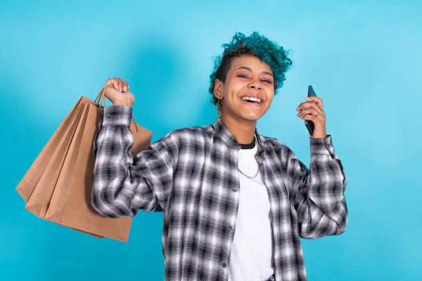 lány vagy nő mosolygós bevásárló táskák és mobiltelefon elszigetelt kék háttér - Fotó, kép