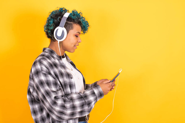 молода брюнетка дівчина з мобільним телефоном та навушниками ізольовані на кольоровому фоні
 - Фото, зображення