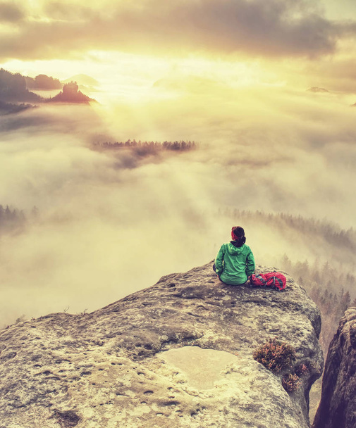 Egyedül utazó nő túrázó ül a szikla szélén, és élvezi a napfelkeltét nézi a völgyet és a hegyeket. Utazó aktív életmód koncepciója - Fotó, kép