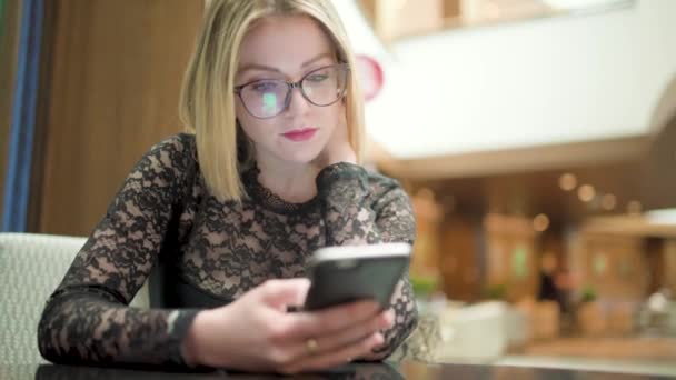 Blonde young woman with glasses using smartphone in shopping mall - Video, Çekim