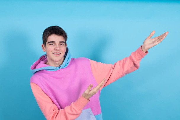 portrait of young teenage man isolated on blue background pointing out - Photo, Image