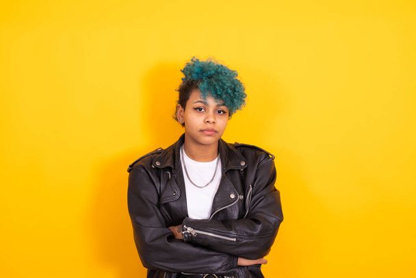 Sarı arka planda mavi saçlı ve deri ceketli Afro Amerikalı genç bir kızın portresi. - Fotoğraf, Görsel