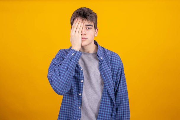 fiatal tinédzser vagy diák fiú elszigetelt színes háttér a kéz, amely a szemet - Fotó, kép