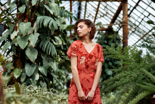 Gyönyörű modell lány a botanikus kertben. Divat stílus smink és piros ruha - Fotó, kép