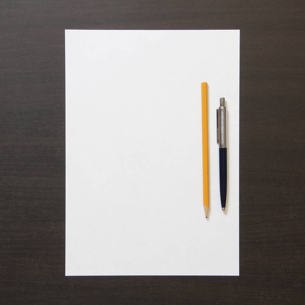 Template of white paper with pen and pencil on dark wenge color wooden background. Concept of business plan and strategy. Stock photo with empty space for text and design. - Foto, Imagem
