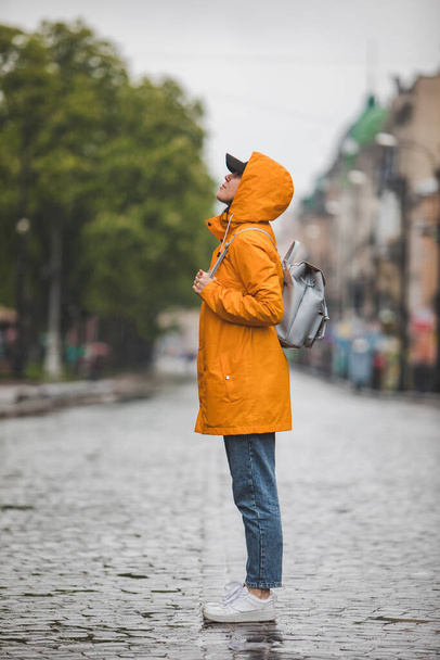 side view of woman in yellow raincoat standing on city street. spring season - Foto, Bild