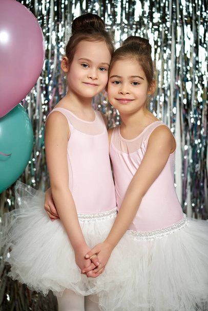 two adorable little girls are posing on the shiny background - Фото, изображение
