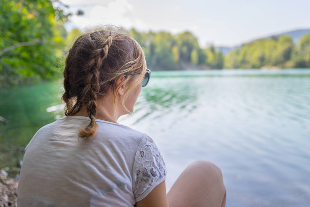 Beautiful young woman is sitting by a lake and enjoying the day - 写真・画像