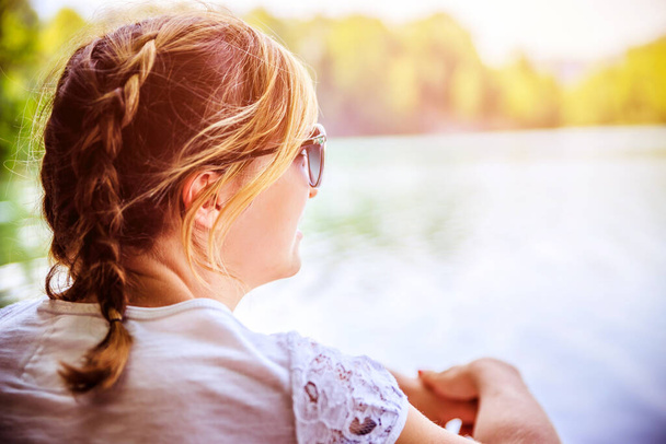 Beautiful young woman is sitting by a lake and enjoying the day - Valokuva, kuva