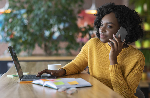 Νεαρή μαύρη επιχειρηματίας έχει συνομιλία με τους πελάτες στο τηλέφωνο - Φωτογραφία, εικόνα