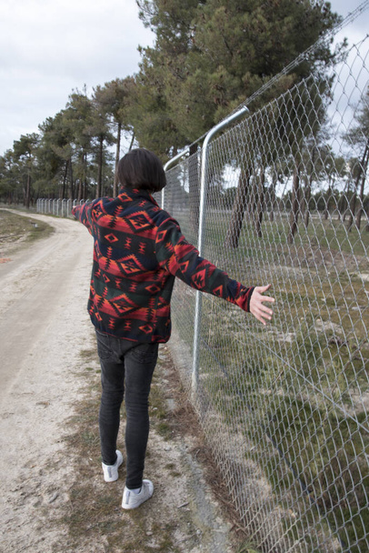Ένας νεαρός που περπατούσε στην πλάτη του σε ένα χωματόδρομο δίπλα σε ένα φράχτη. - Φωτογραφία, εικόνα