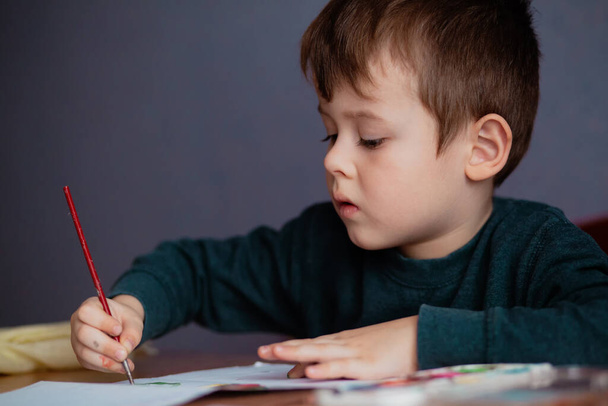 Little boy draws a brush and paint his first picture. Closeup portrait of cute little boy drawing picture. - Foto, immagini