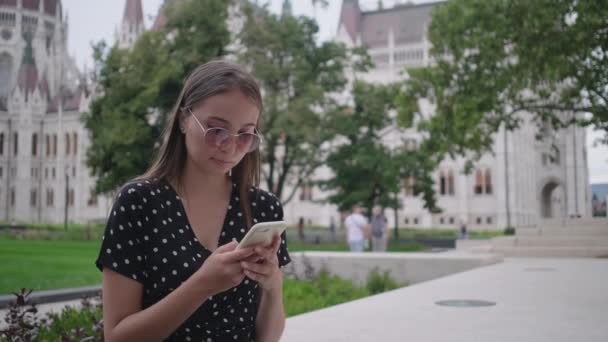 młoda kobieta wysyła wiadomość przez telefon komórkowy na zewnątrz - Materiał filmowy, wideo