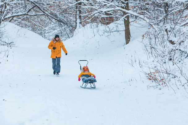 отец с дочерью в желтых зимних пальто скольжения снежный холм семейное время - Фото, изображение
