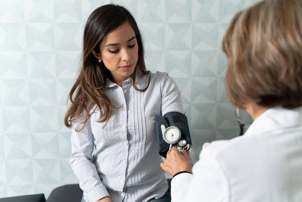 Ginecologista feminina sênior verificando mulher com medidor de pressão arterial no hospital
 - Foto, Imagem