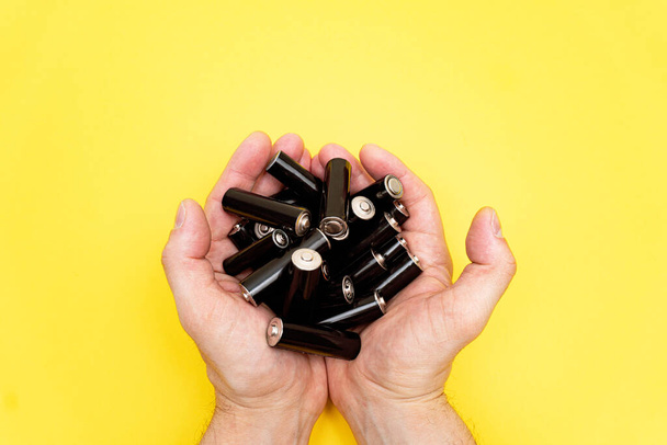 Pile of black aa batteries in mans handful on yellow background. - Fotó, kép