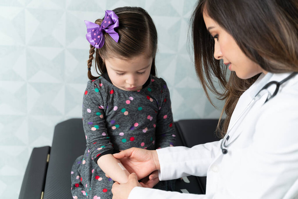 Dívka při pohledu na ženské pediatr nanášení lepicí obvaz na ruce na klinice - Fotografie, Obrázek