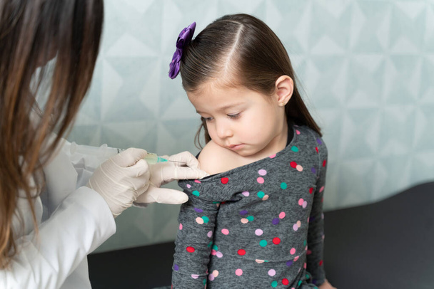 Naislääkäri pistämällä käsivarteen söpö valkoihoinen tyttö rokotteen klinikalla
 - Valokuva, kuva