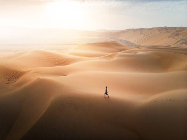 Kobieta spacerująca po pustynnych wydmach widok z powietrza o zachodzie słońca - Zdjęcie, obraz