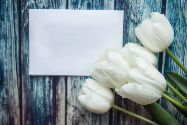 Bílé tulipány a bílá maketa prázdné na modrém dřevěném pozadí. Byt ležel, horní pohled, kopírovací prostor - Fotografie, Obrázek