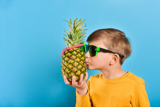 Мальчик в очках держит ананас и целует его как друга.
. - Фото, изображение
